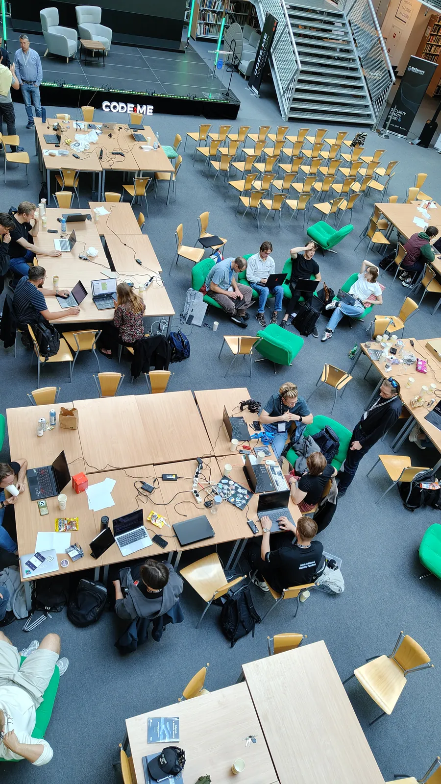 Widok z góry na stoły hackathonu, laptopy i pracujące zespoły w hali biblioteki