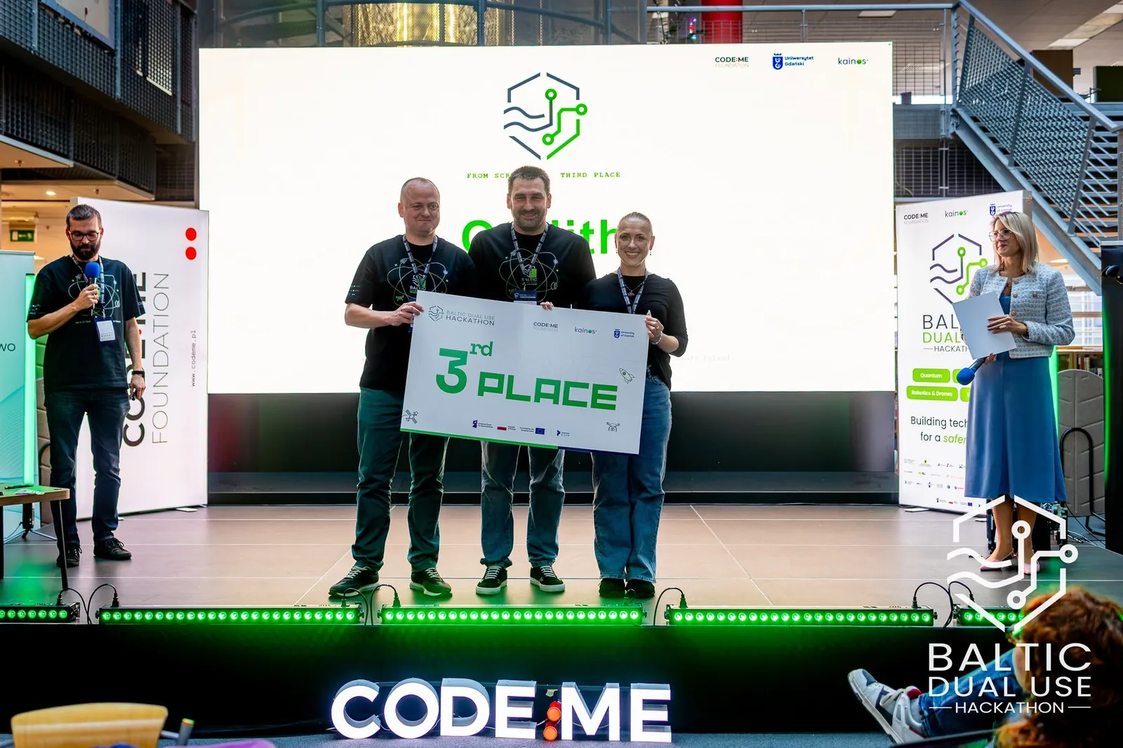 Zespół OTOLITH na scenie Baltic Dual Use Hackathon z planszą 3rd PLACE, w tle ekran z logo OTOLITH