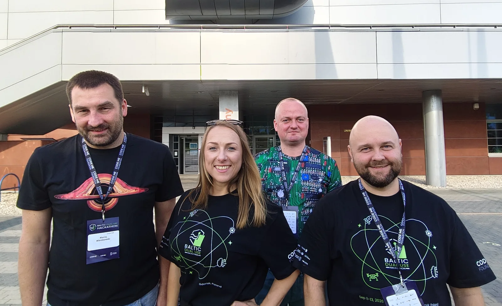 Czteroosobowy zespół OTOLITH w koszulkach Baltic Dual Use Hackathon przed budynkiem Uniwersytetu Gdańskiego