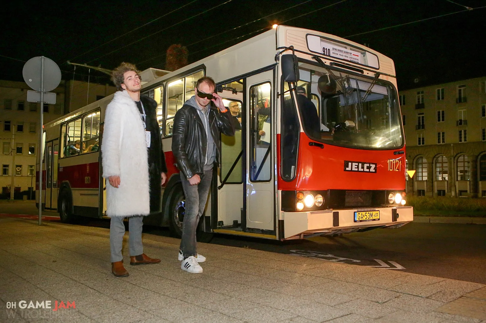 Dwóch uczestników w futrach i okularach przed trolejbusem nocą