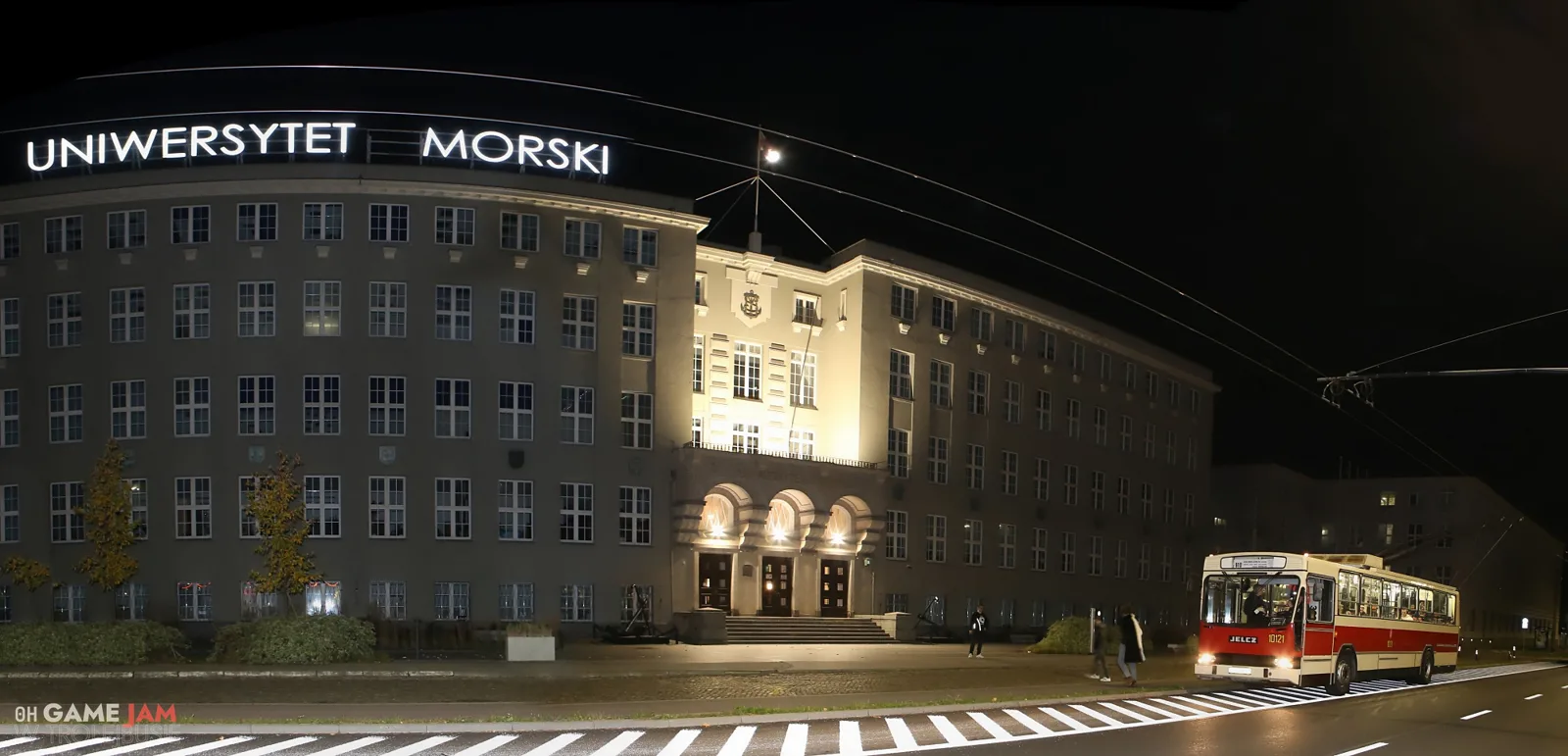 Nocna panorama: oświetlony gmach Uniwersytetu Morskiego w Gdyni i czerwono-kremowy trolejbus na ulicy