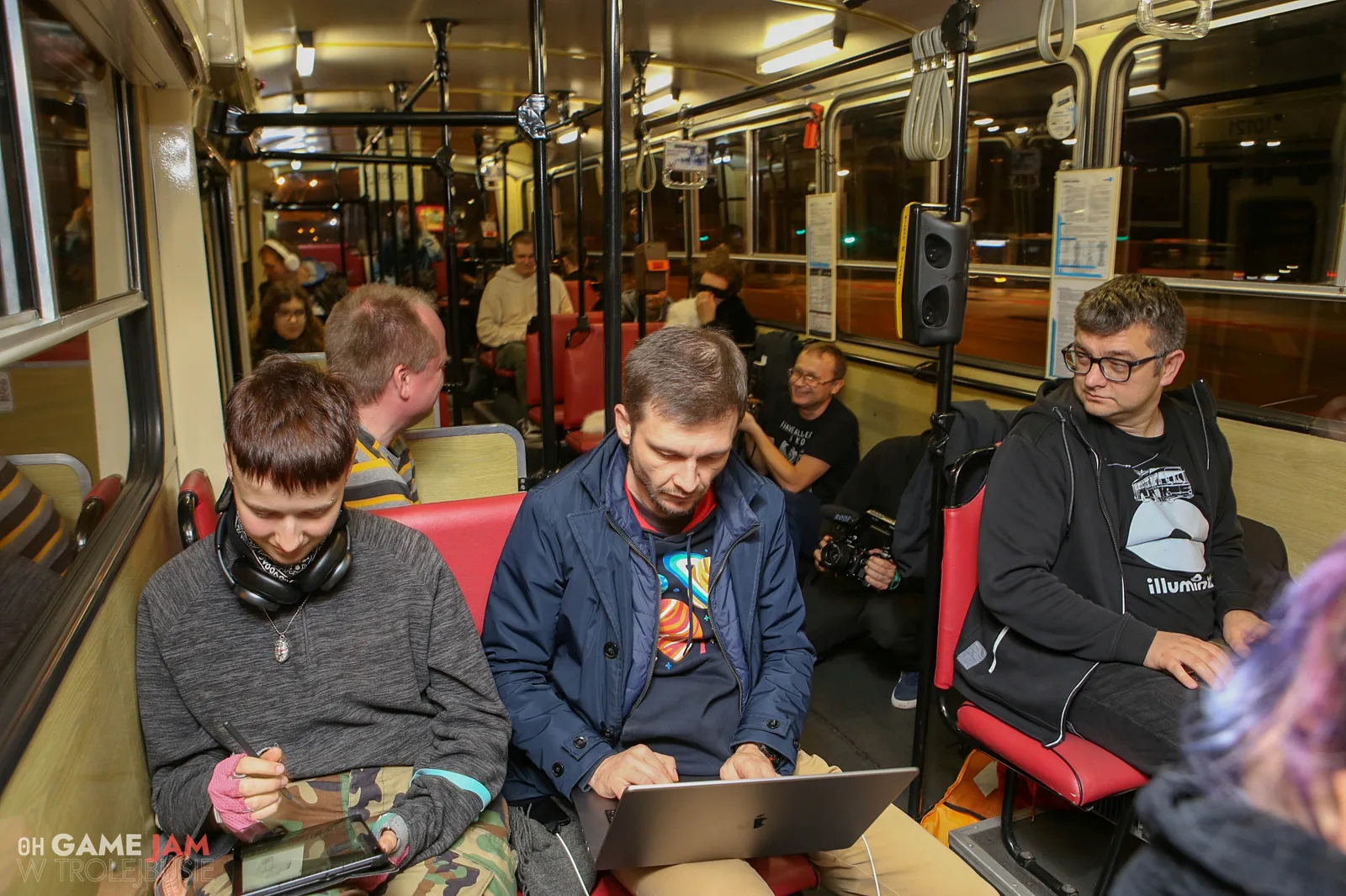Wnętrze trolejbusu nocą: uczestnicy game jamu z laptopami na kolanach