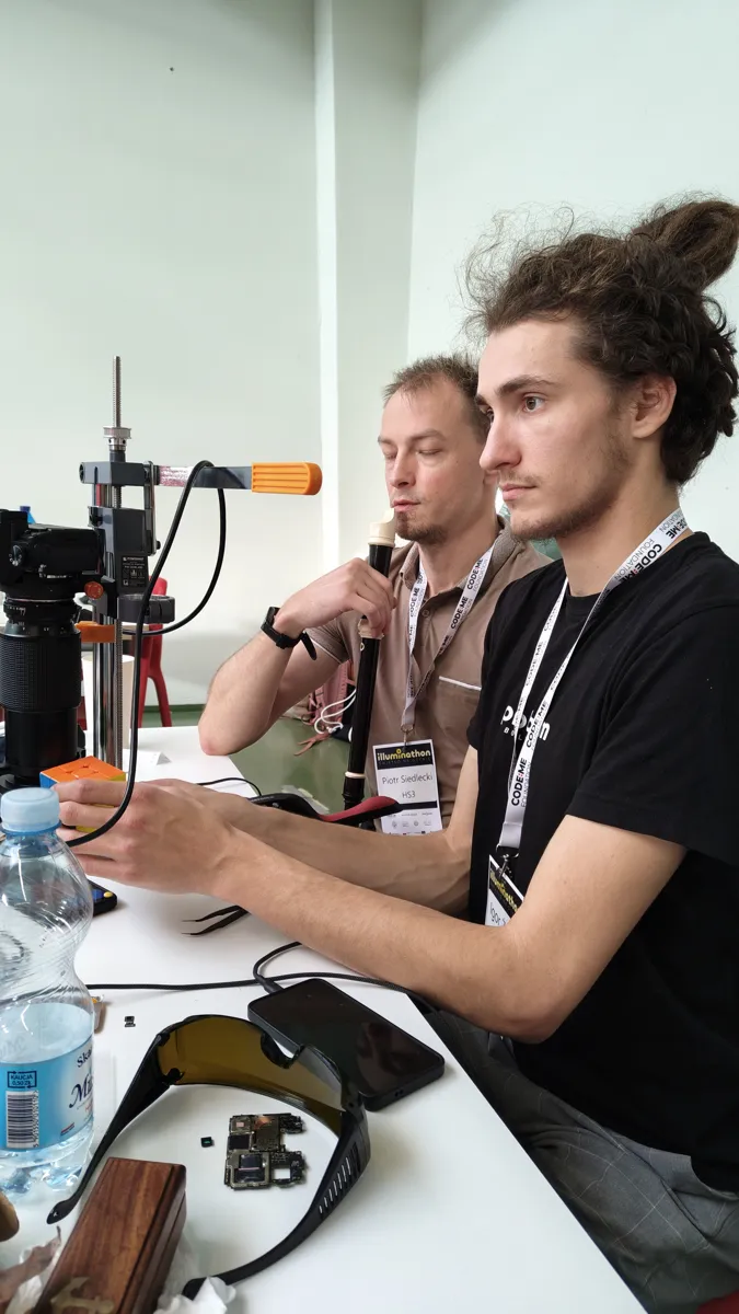 Dwóch członków zespołu SWAG 3000 przy stanowisku z mikroskopem i elektroniką, skupieni na pracy