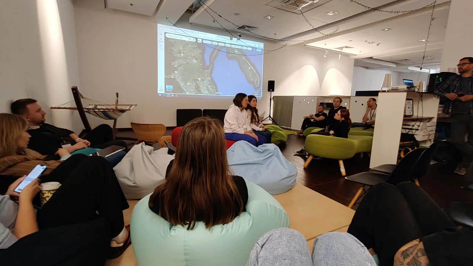 Uczestnicy maratonu na pufach i krzesłach w sali coworkingu PPNT, na ekranie mapa